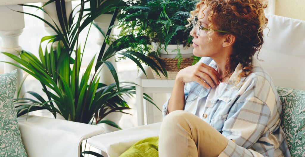 Woman near plants curled up in a chair thinking about change