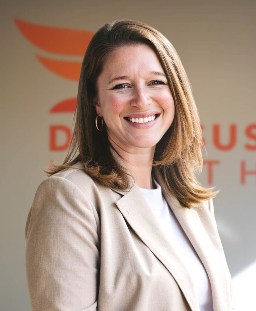 Headshot of Elaine Calip, Diversus Health Chief Experience officer, standing in front of orange Diversus Health logo